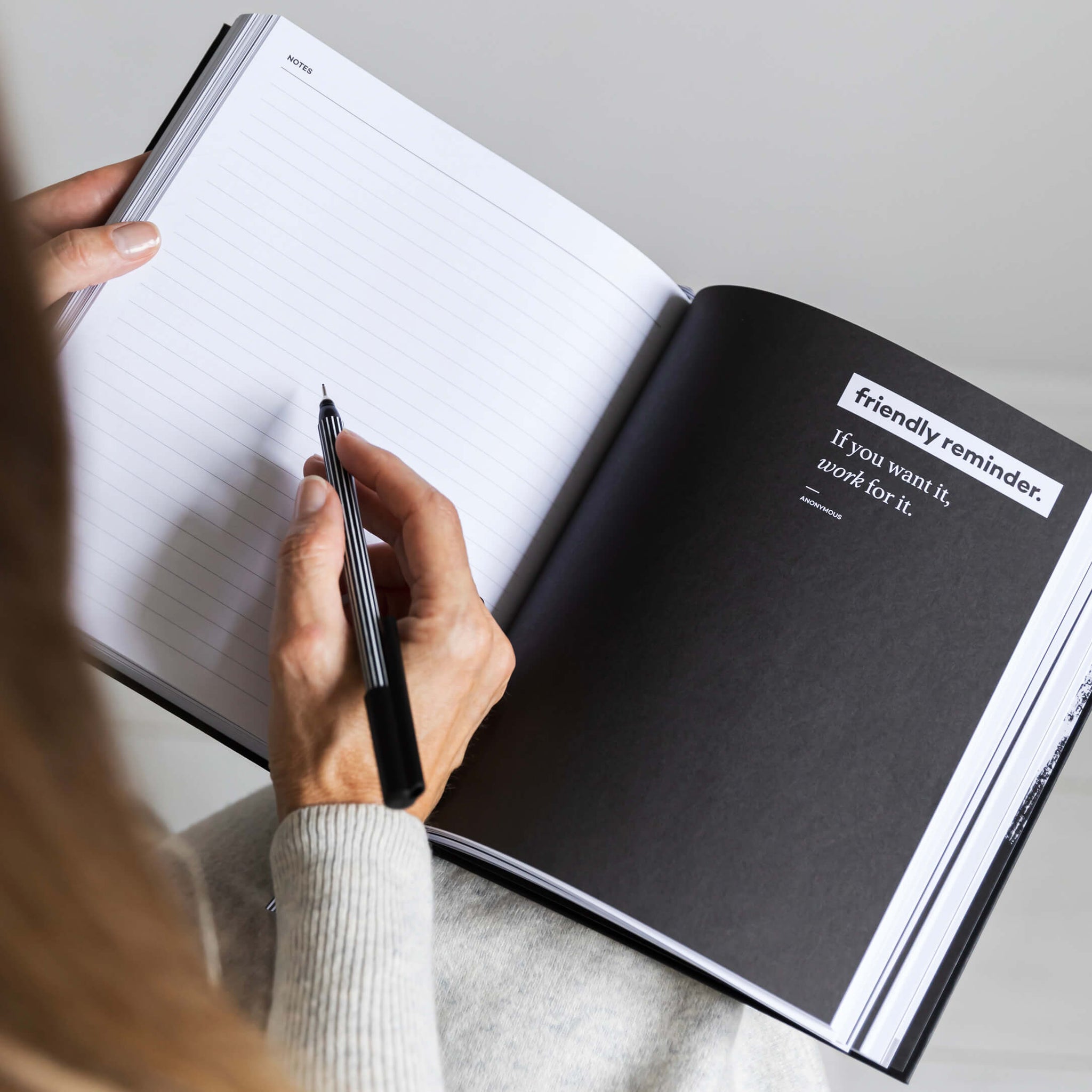 Woman writing in a HELLO TIME planner open to a motivational quote page that reads, “If you want it, work for it.” Focused and ready to plan big.