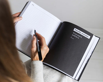 Woman writing in a HELLO TIME planner open to a motivational quote page that reads, “If you want it, work for it.” Focused and ready to plan big.