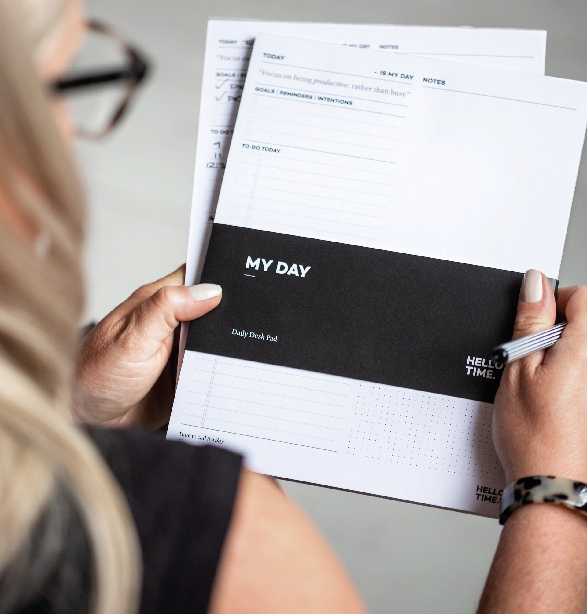 Woman holding the HELLO TIME ‘My Day’ daily desk pad with pen in hand — ready to plan, focus and take on the day with intention.