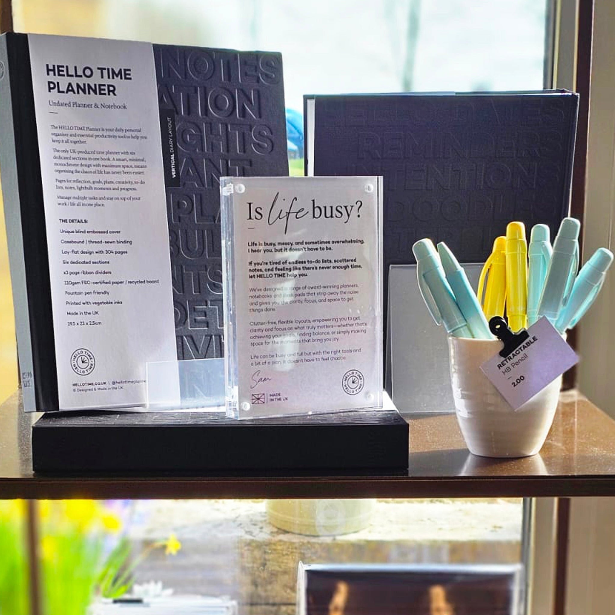 A HELLO TIME planner display with pens and an ‘Is life busy?’ sign — inspiring calm, clarity, and better days through thoughtful design.