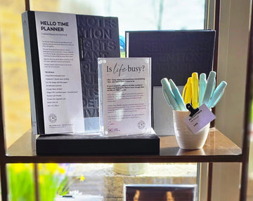 A HELLO TIME planner display with pens and an ‘Is life busy?’ sign — inspiring calm, clarity, and better days through thoughtful design.