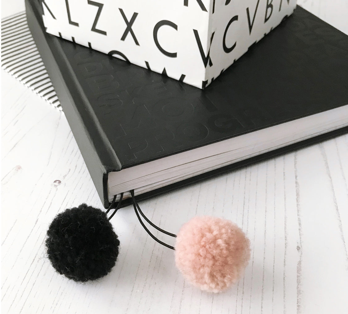 Black HELLO TIME planner with playful black and blush pom-pom bookmarks — a stylish mix of productivity and personality for your desk.