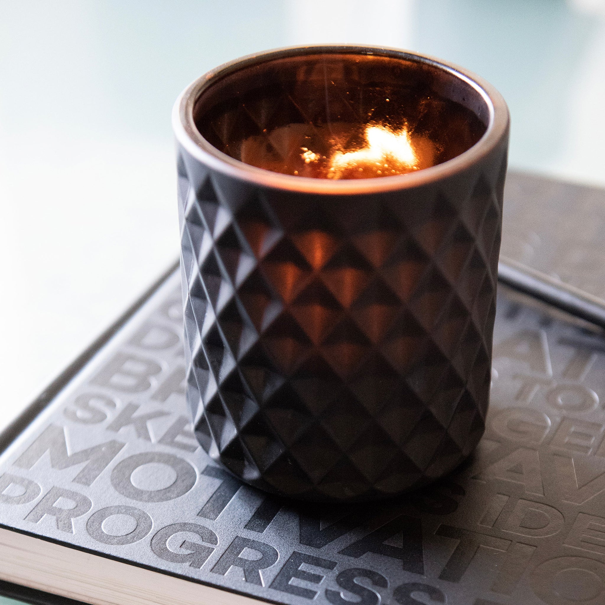 A lit candle in a textured black holder resting on a HELLO TIME planner — sparking focus, calm, and creative motivation.