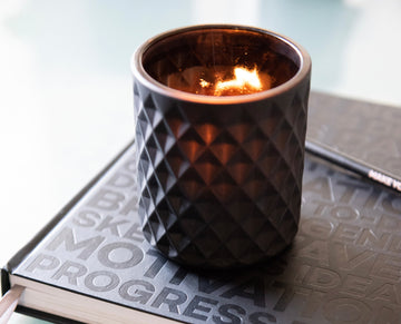 A lit candle in a textured black holder resting on a HELLO TIME planner — sparking focus, calm, and creative motivation.