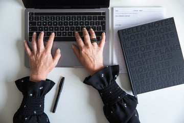 Woman planning her month using the HELLO TIME planner at a bright desk with laptop, coffee, and camera gear — calm focus meets creative energy.