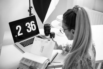 Woman planning her month using the HELLO TIME planner at a bright desk with laptop, coffee, and camera gear — calm focus meets creative energy.