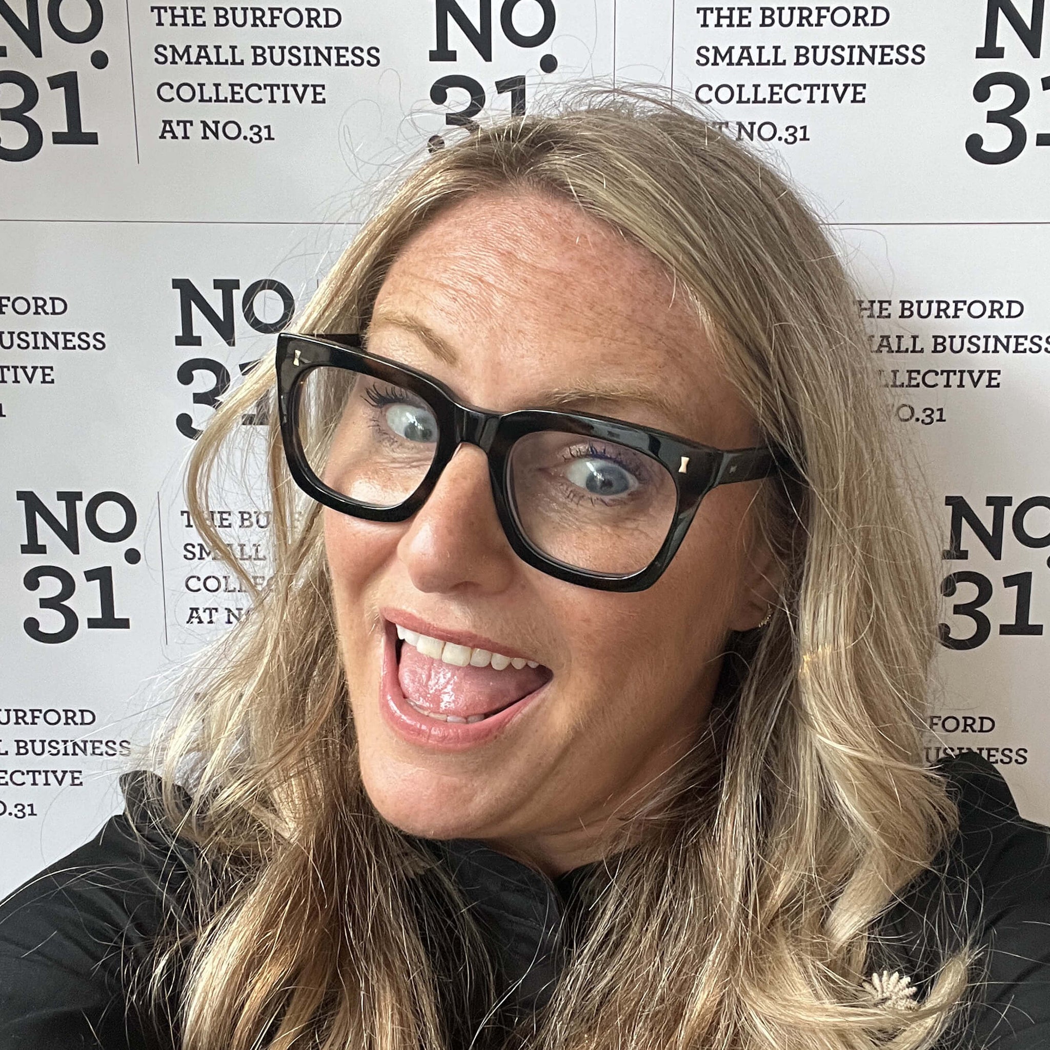 Smiling woman at The Burford Small Business Collective No.31 event, standing in front of branded backdrop, full of positive energy and personality.