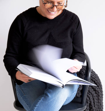 Woman smiling while flicking through the HELLO TIME planner, dressed in a black jumper and jeans — planning that feels good.