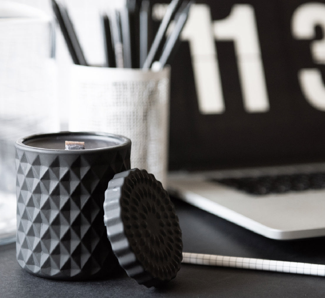 Black textured candle with lid beside monochrome desk accessories and a digital clock — creating calm, focus and style in your workspace.