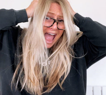 Woman with long blonde hair and glasses holding her head and laughing in frustration — the face of a busy day we all know too well.