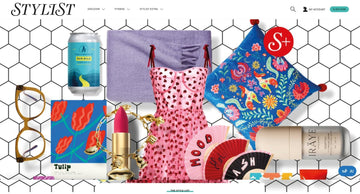 Colourful flat lay of fashion and lifestyle items featured in Stylist magazine, including a pink heart dress, bold prints, and beauty products.