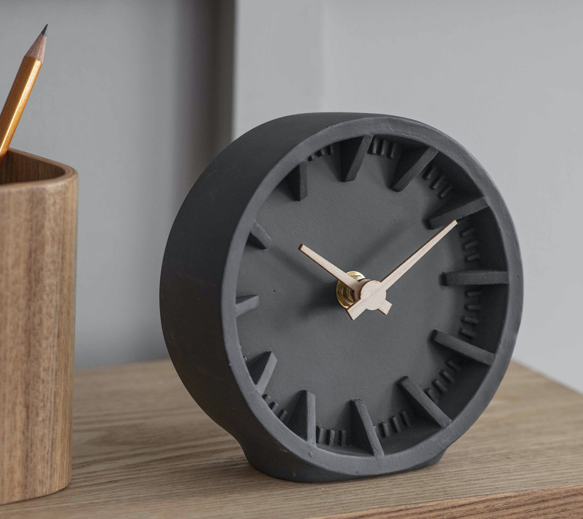 Minimalist dark grey desk clock with wooden hands, sitting on a light wood surface beside a pencil pot — calm, modern, and perfectly on time.