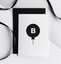 Monochrome birthday card with black balloon and letter B initial, shown with ribbon.