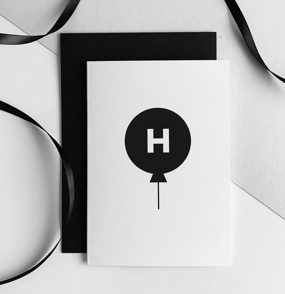 White children’s birthday card with black balloon and letter H initial, paired with black envelope.