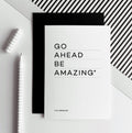 White greetings card with text “Go Ahead Be Amazing” shown with black envelope and pen.