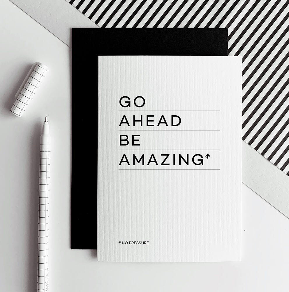 White greetings card with text “Go Ahead Be Amazing” shown with black envelope and pen.