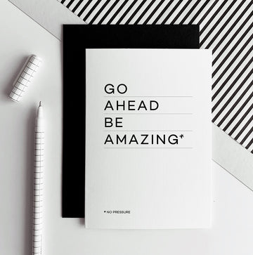 White greetings card with text “Go Ahead Be Amazing” shown with black envelope and pen.