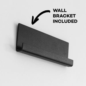 Black metal wall bracket mounted on white wall with text stating bracket included