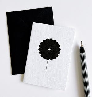 White greeting card featuring single bold black flower illustration, paired with envelope and pen.