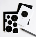 Two white cards, one with single black flower and one with multiple flowers, displayed with envelope and pen.