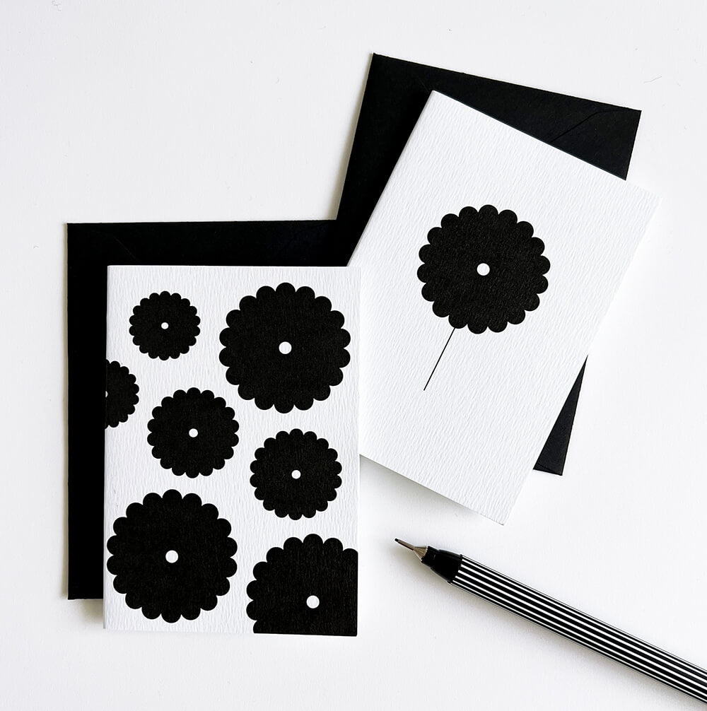 Two white cards, one with single black flower and one with multiple flowers, displayed with envelope and pen.