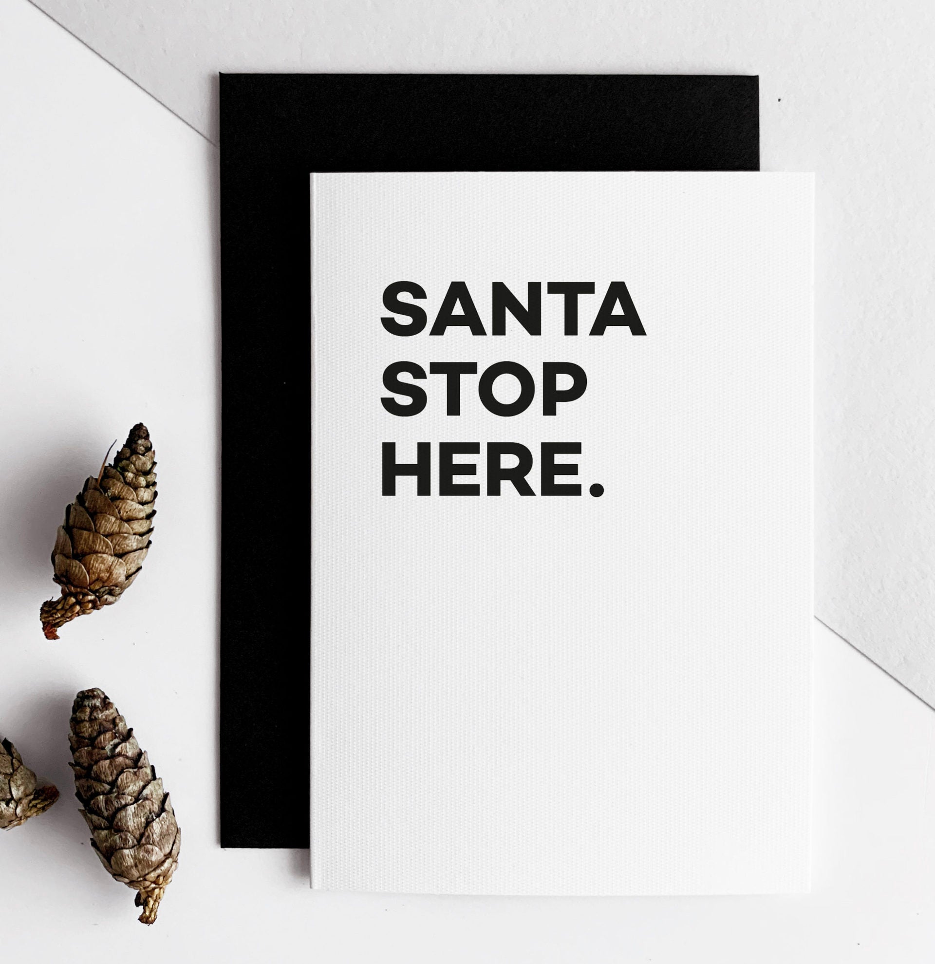 Minimal white Christmas card with bold black text reading “Santa Stop Here.”