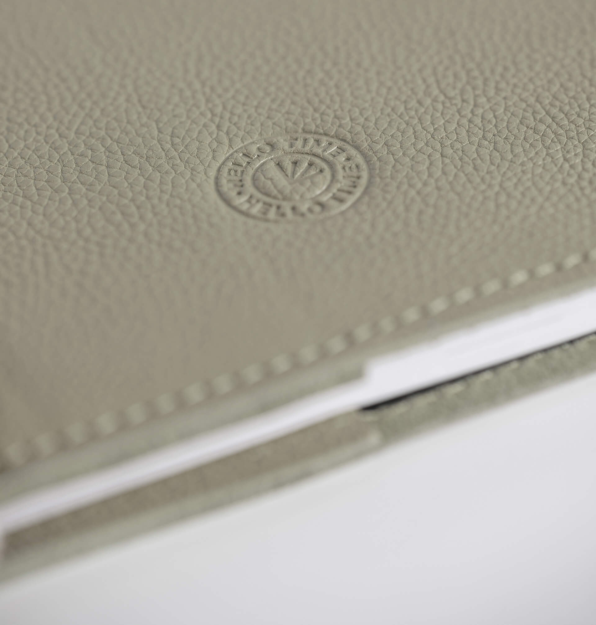 Close-up of a textured beige leather notebook with HELLO TIME logo on a white background