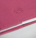 Close-up of a candy pink leather notebook with HELLO TIME logo on a white background