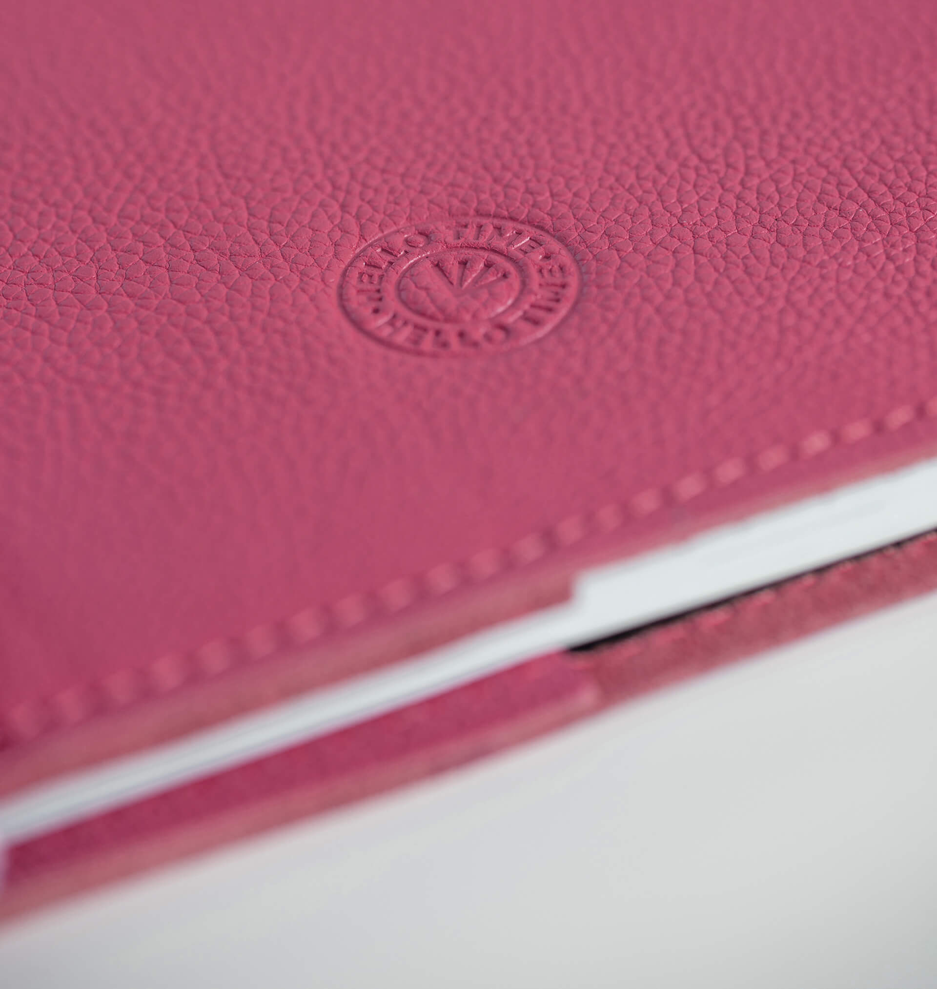 Close-up of a candy pink leather notebook with HELLO TIME logo on a white background