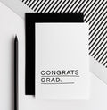 White greeting card with black text reading Congrats Grad, paired with a black envelope.