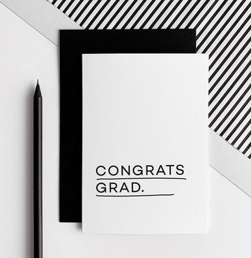 White greeting card with black text reading Congrats Grad, paired with a black envelope.