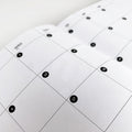 Close-up of black circular date dot stickers on undated monthly calendar spread