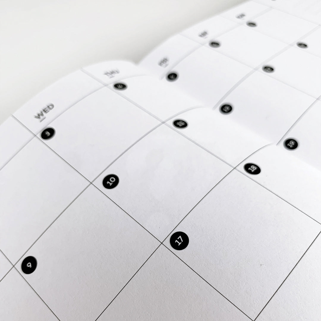 Close-up of black circular date dot stickers on undated monthly calendar spread