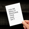 Hand holding monochrome Rocking Dad card with bold typographic message.