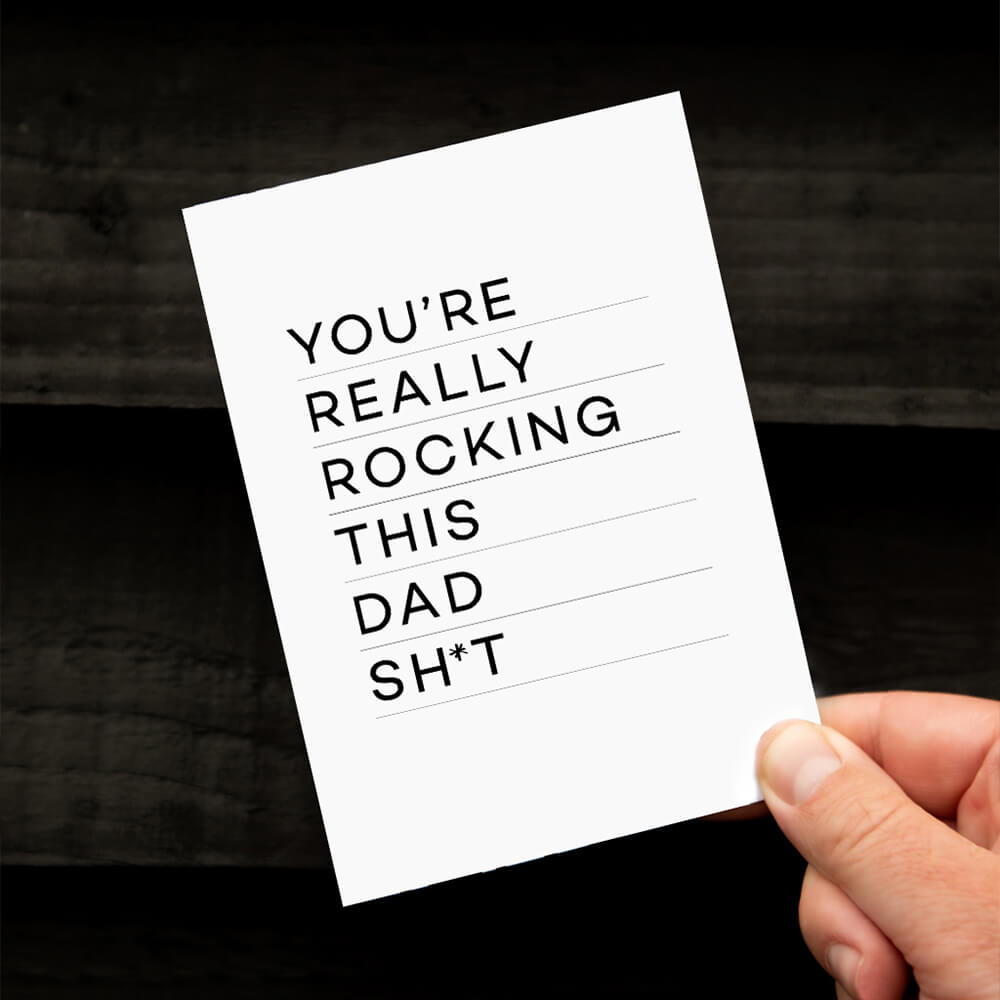 Hand holding monochrome Rocking Dad card with bold typographic message.