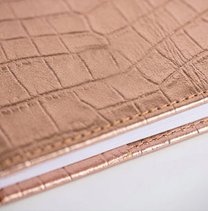 Close-up of rose gold croc-embossed leather HELLO TIME notebook cover texture.