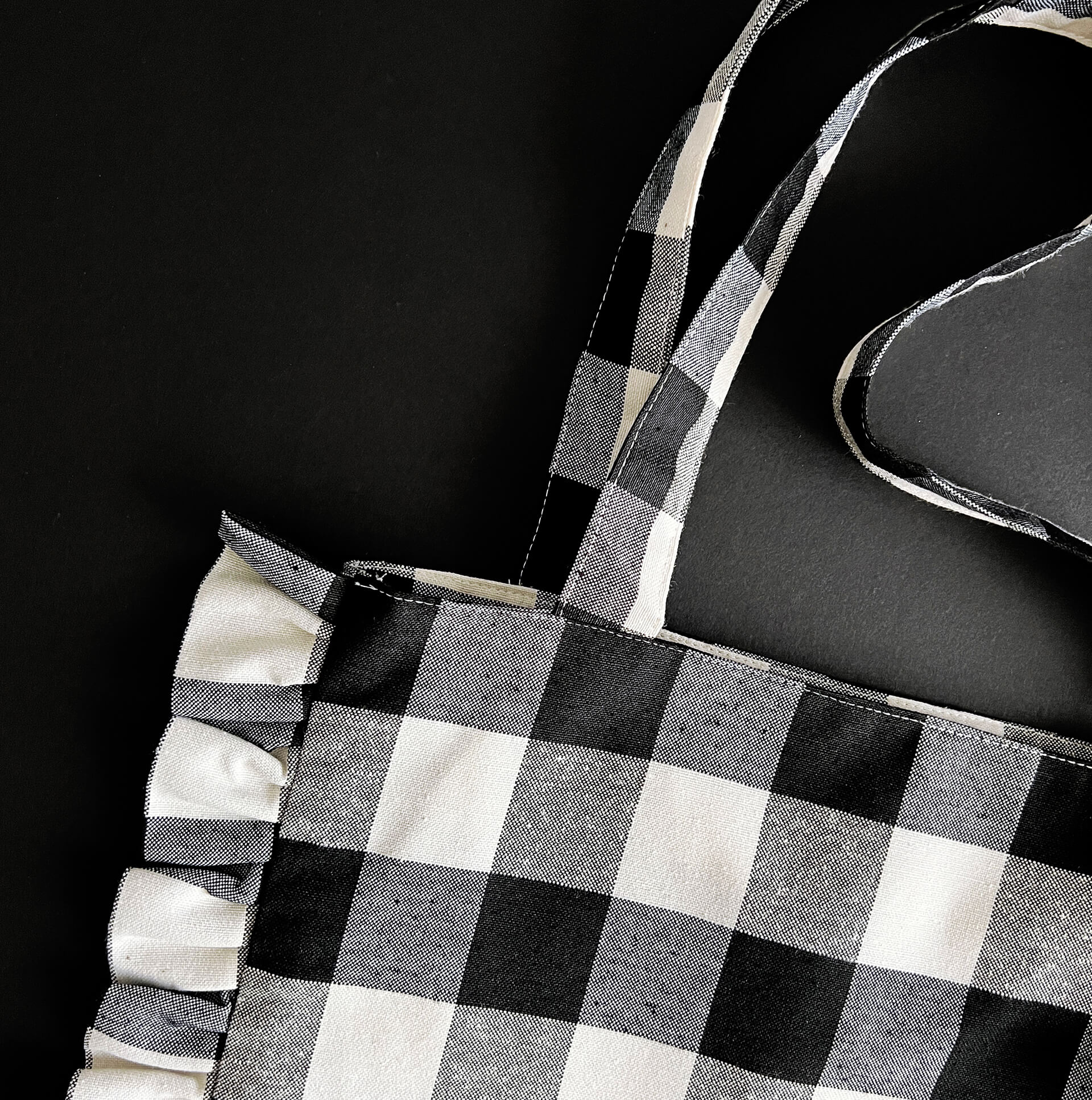 Top corner of black and white ruffle tote bag with gingham pattern and fabric handles

