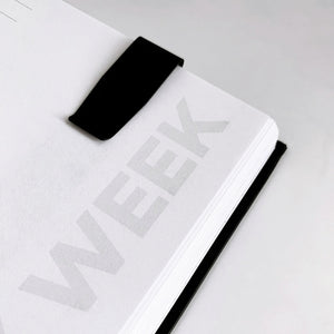 Black clip bookmark attached to the top of a planner page labeled “WEEK”