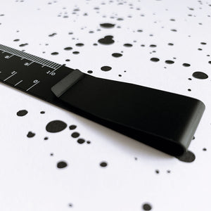 Black ruler bookmark with clip on a white notebook with black ink splatter pattern