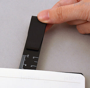 Hand holding a black ruler bookmark clipped to the edge of a notebook page