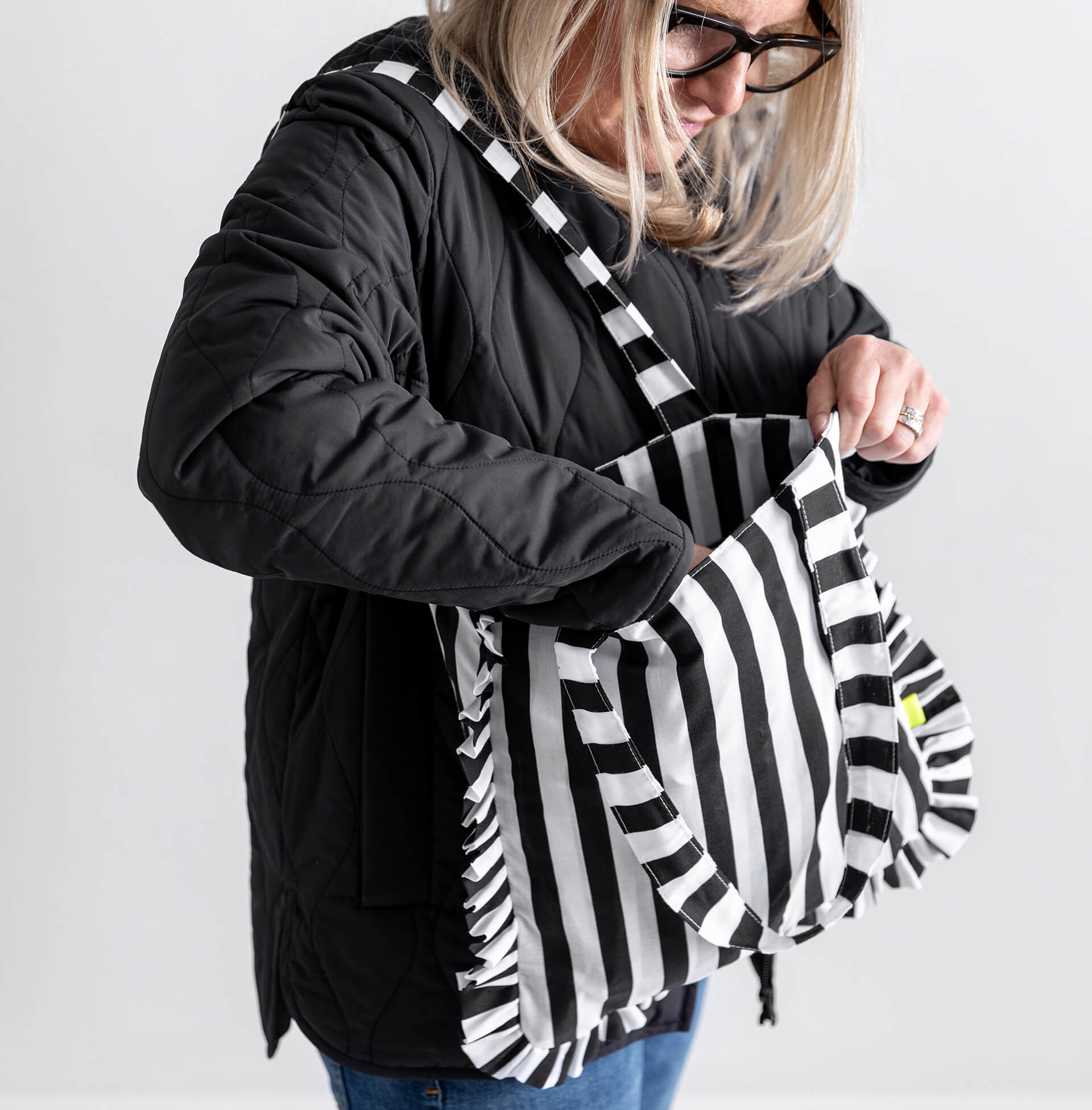 Woman in black coat reaching into black and white striped HELLO TIME tote bag with ruffle edges