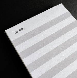 Close-up of HELLO TIME striped braindump to-do pad with light grey and white lines on black background