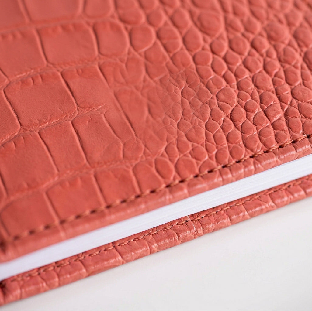Close-up of coral croc-embossed leather HELLO TIME notebook cover texture.