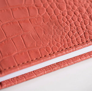 Close-up of coral croc-embossed leather HELLO TIME notebook cover texture.