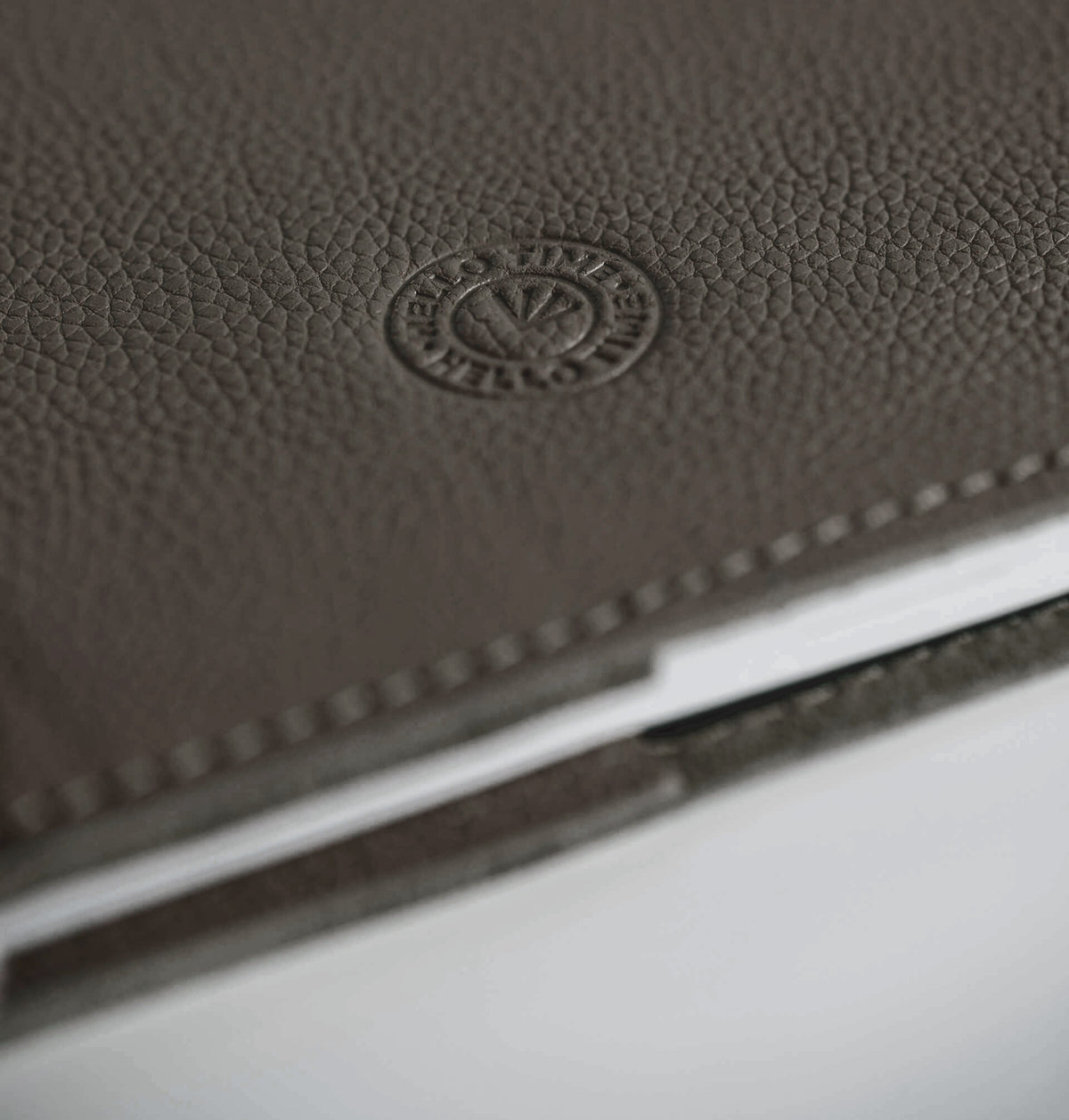 Close-up of greige leather HELLO TIME notebook cover with embossed circular logo stamp.