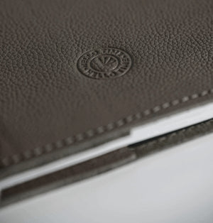 Close-up of greige leather HELLO TIME notebook cover with embossed circular logo stamp.