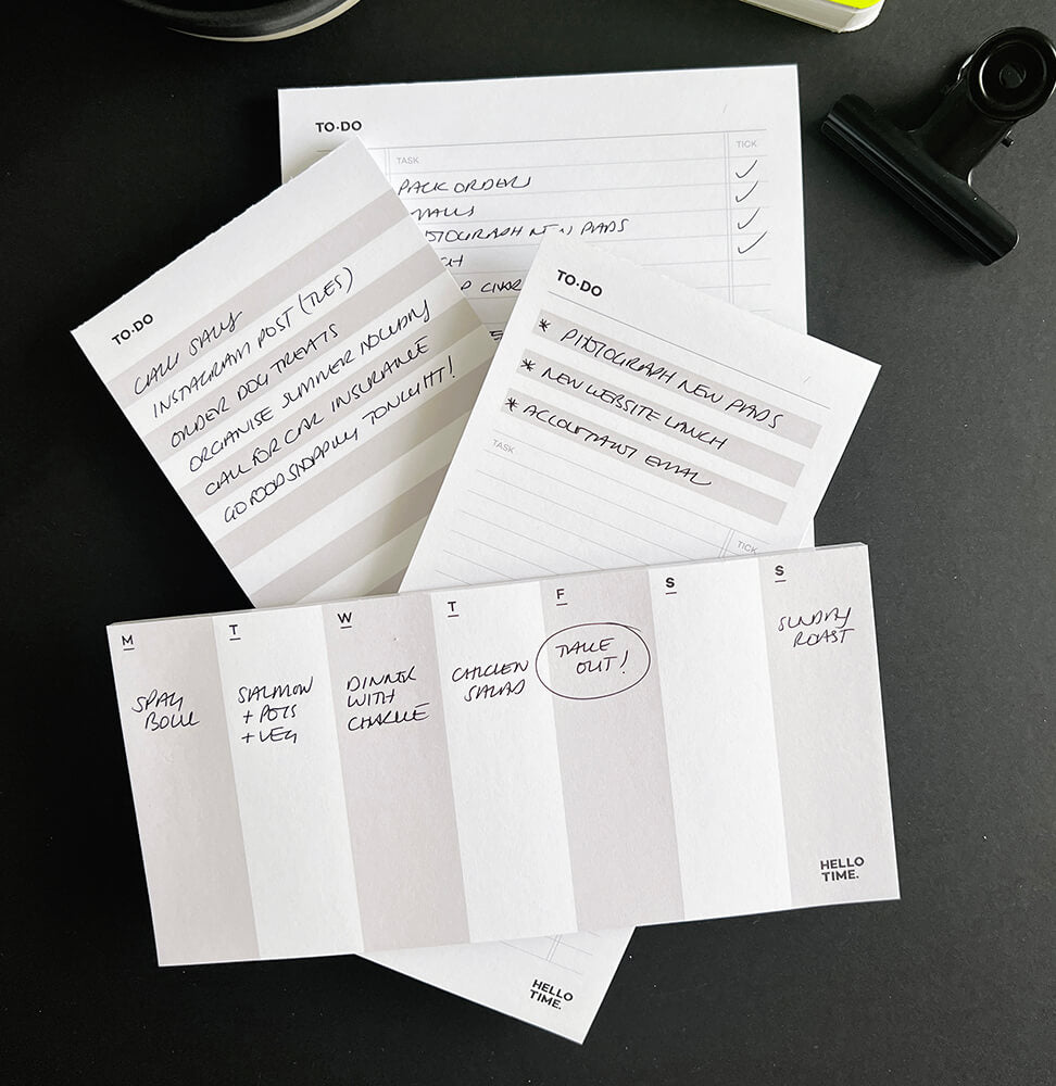 Flat lay of HELLO TIME desk pads including time-task, braindump, weekly, and mini list pads, with handwritten notes on each.