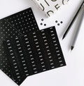 Two black HELLO TIME diary sticker sheets with white months and dates, shown with pens and monochrome packaging