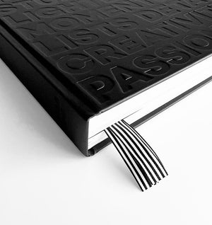 Close-up of HELLO TIME black planner corner showing embossed cover words and black-and-white striped ribbon bookmarks