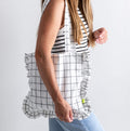 Woman carrying HELLO TIME tote bag in black and white grid print with ruffled edges